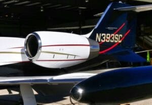 Jet aircraft tail with a sleek design, featuring a prominent engine and registration number N393SC against a hangar backdrop.