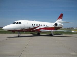 A sleek white and red private jet parked on a tarmac under a clear blue sky.