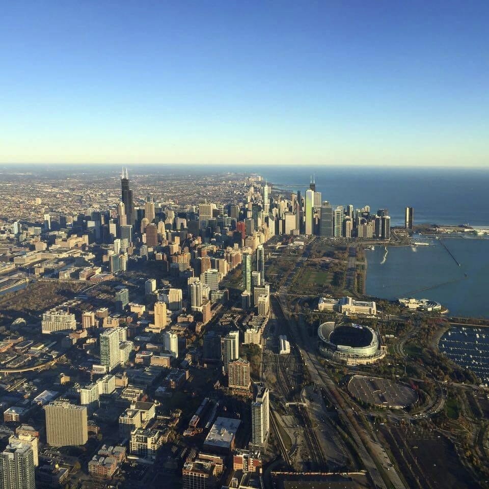 Aerial view of Chicago's skyline, featuring tall buildings, Lake Michigan, and a clear blue sky.