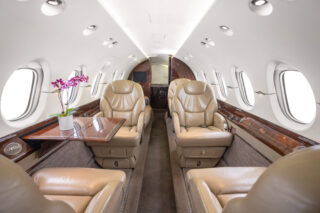 Luxurious private jet interior featuring beige leather seats, wooden accents, and a small orchid on a polished table.