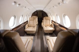 Luxurious private jet interior featuring beige leather seats, large windows, and a sleek, modern design.