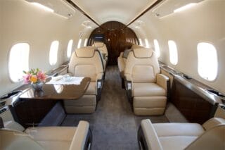 Luxurious private jet interior featuring beige leather seats, a polished wooden table, and a floral centerpiece.
