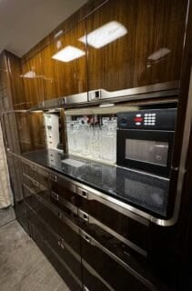 Sleek kitchen cabinetry with a microwave, crystal glassware, and a polished black countertop in a modern design.