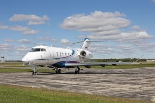 A sleek private jet parked on a runway under a blue sky with fluffy clouds and green grass nearby.