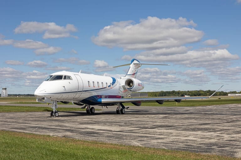 A sleek private jet parked on a runway under a blue sky with fluffy clouds and green grass nearby.