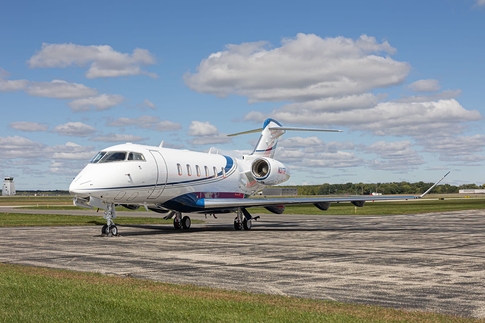 A sleek private jet parked on a runway under a blue sky with fluffy clouds and green grass nearby.