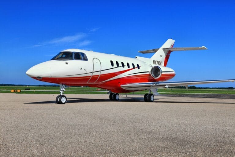 A sleek private jet with a white and red design parked on a tarmac under a clear blue sky.