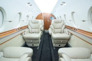 Luxurious private jet interior featuring plush leather seats, large windows, and elegant wood accents.