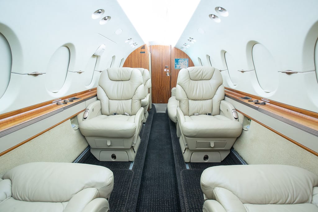 Luxurious private jet interior featuring plush leather seats, large windows, and elegant wood accents.