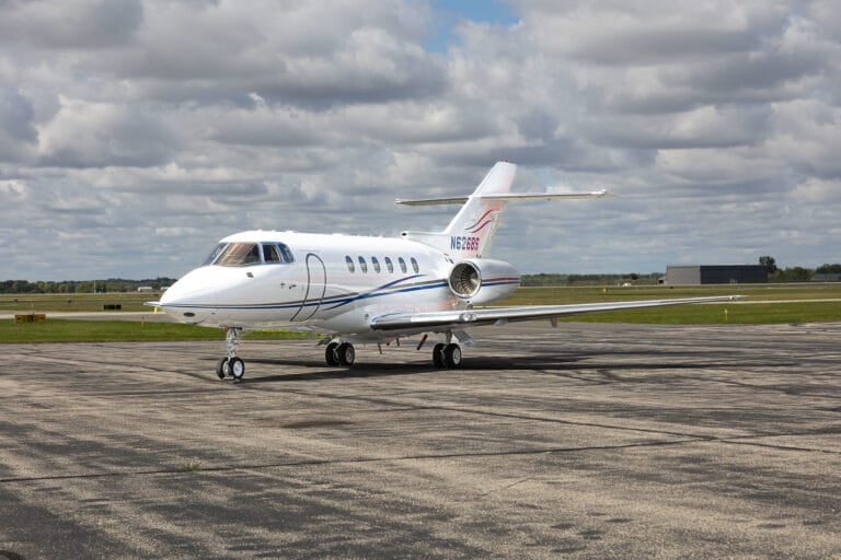 A sleek white private jet with blue and red accents parked on a tarmac under a cloudy sky.
