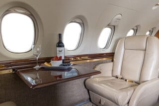 Luxurious airplane interior featuring a leather seat, wine bottle, glass, and a platter of fruits on a polished table.