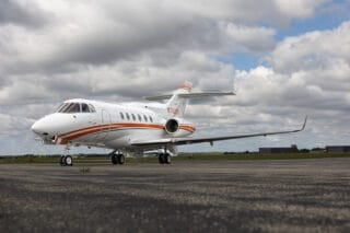 A sleek white jet with orange stripes parked on a runway under a cloudy sky.
