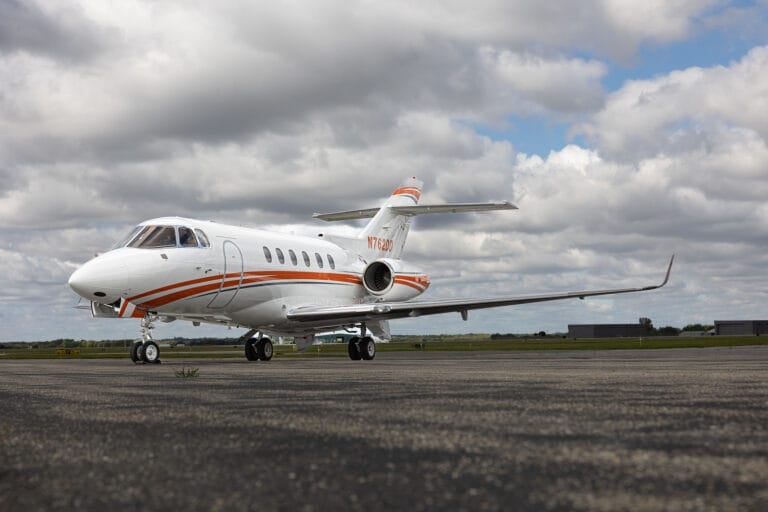 A sleek white jet with orange stripes parked on a runway under a cloudy sky.