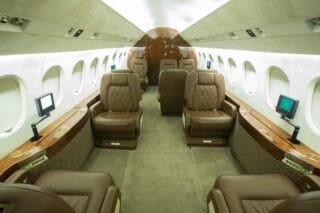 Luxurious private jet interior featuring plush brown leather seats, wooden accents, and individual entertainment screens.