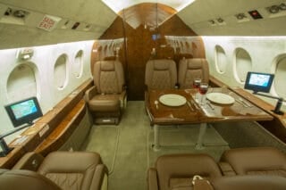 Luxurious private jet interior featuring plush leather seats, a polished wooden table set for dining, and personal screens.