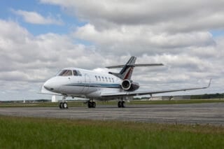 A sleek private jet on a tarmac, with a cloudy sky and green grass in the foreground.