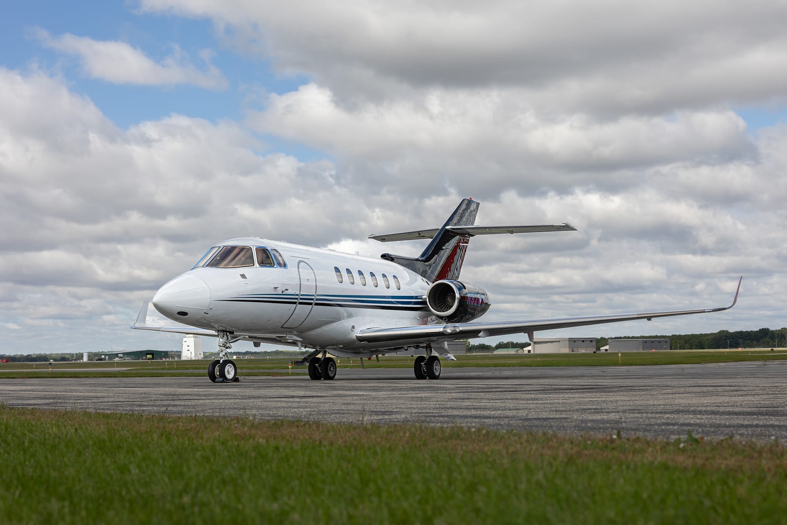 A sleek private jet on a tarmac, with a cloudy sky and green grass in the foreground.