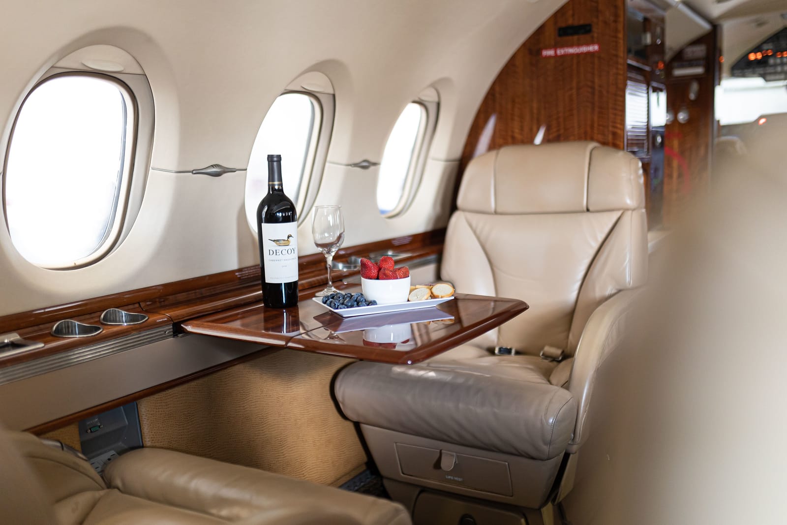 Luxurious airplane interior featuring a bottle of wine, glass, and a plate of strawberries and blueberries on a table.