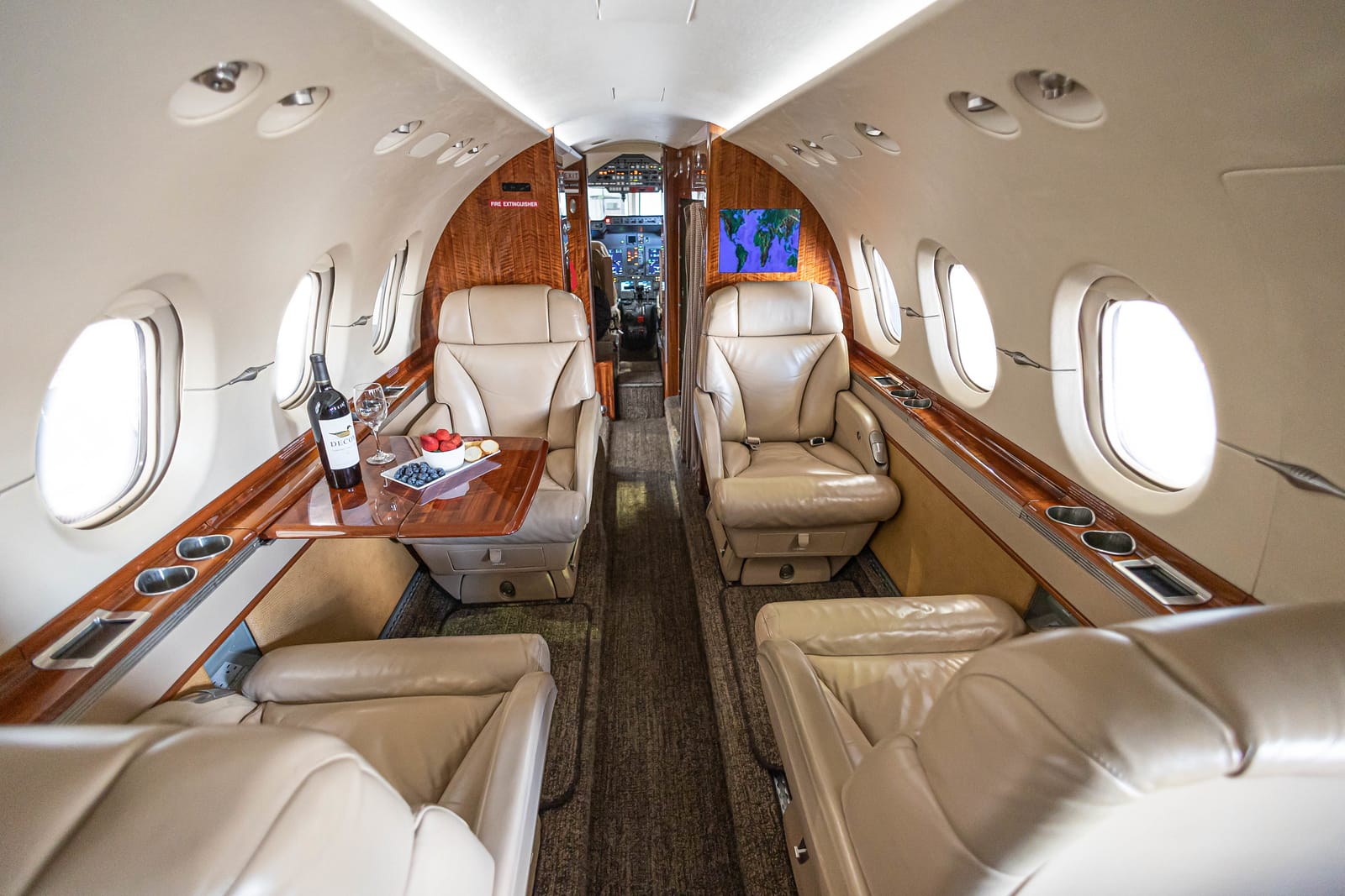 Luxurious private jet interior featuring leather seats, a wooden table with wine and fruit, and large windows.