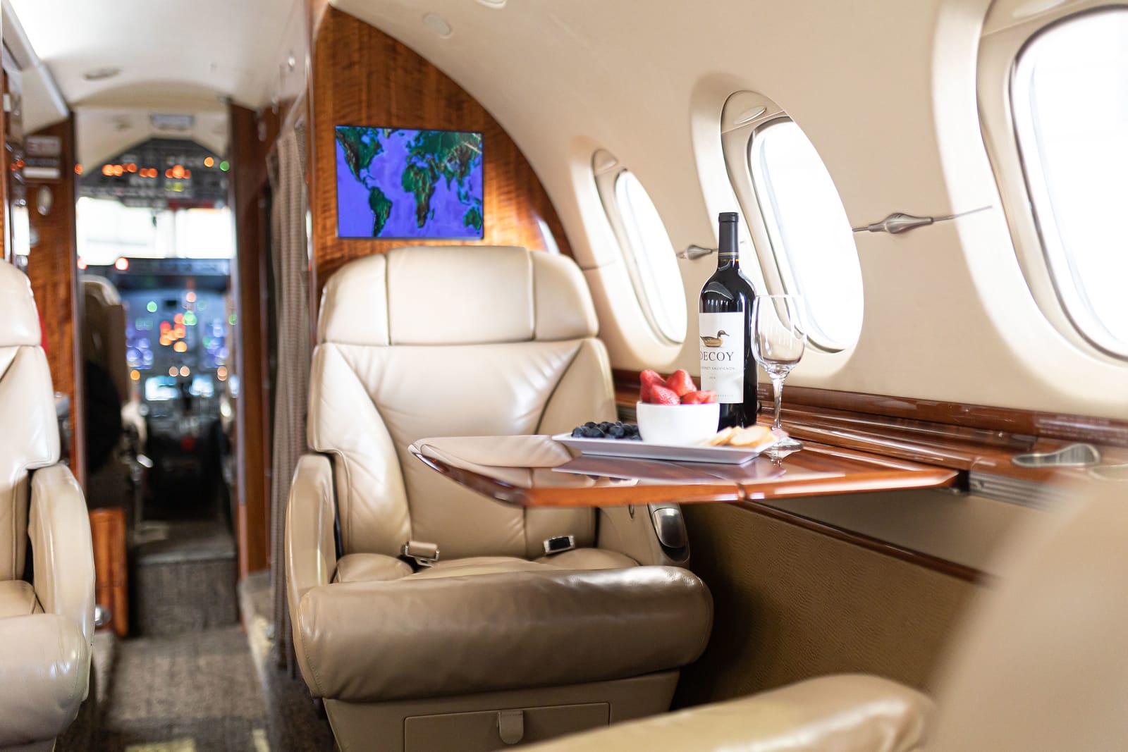 Luxurious private jet interior featuring leather seats, a table with wine, fruit, and a map display in the background.