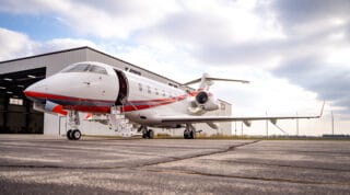 A sleek private jet with red accents parked on a tarmac beside a hangar under a cloudy sky.