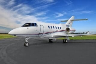 A sleek white private jet with blue skies and green grass in the background, parked on a tarmac.