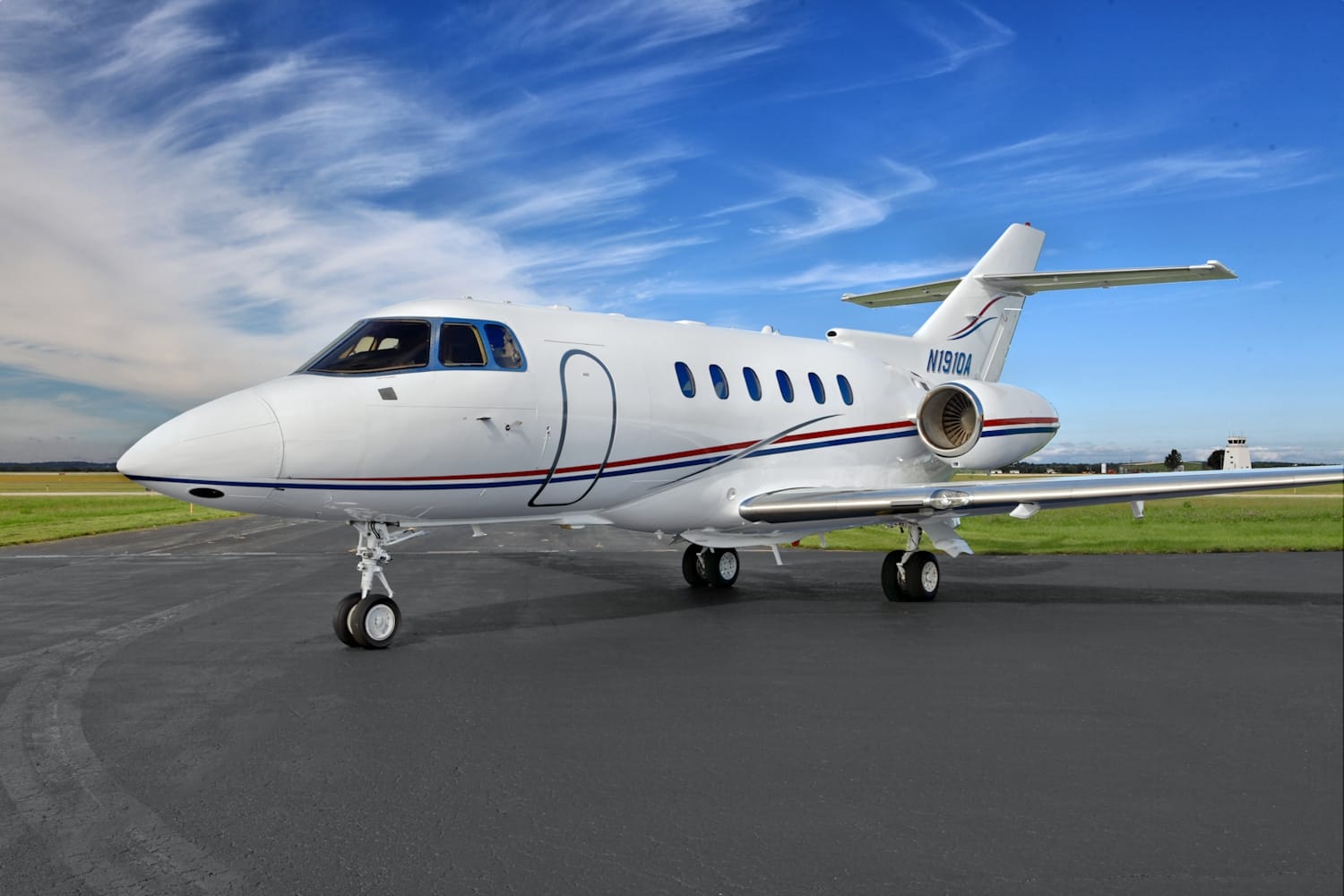 A sleek white private jet with blue skies and green grass in the background, parked on a tarmac.