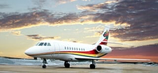 A sleek private jet with a colorful tail design parked on an airport runway against a vibrant sunset sky.