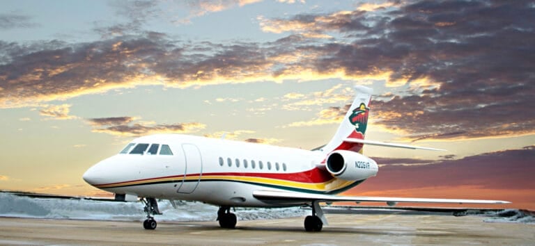 A sleek private jet with a colorful tail design parked on an airport runway against a vibrant sunset sky.