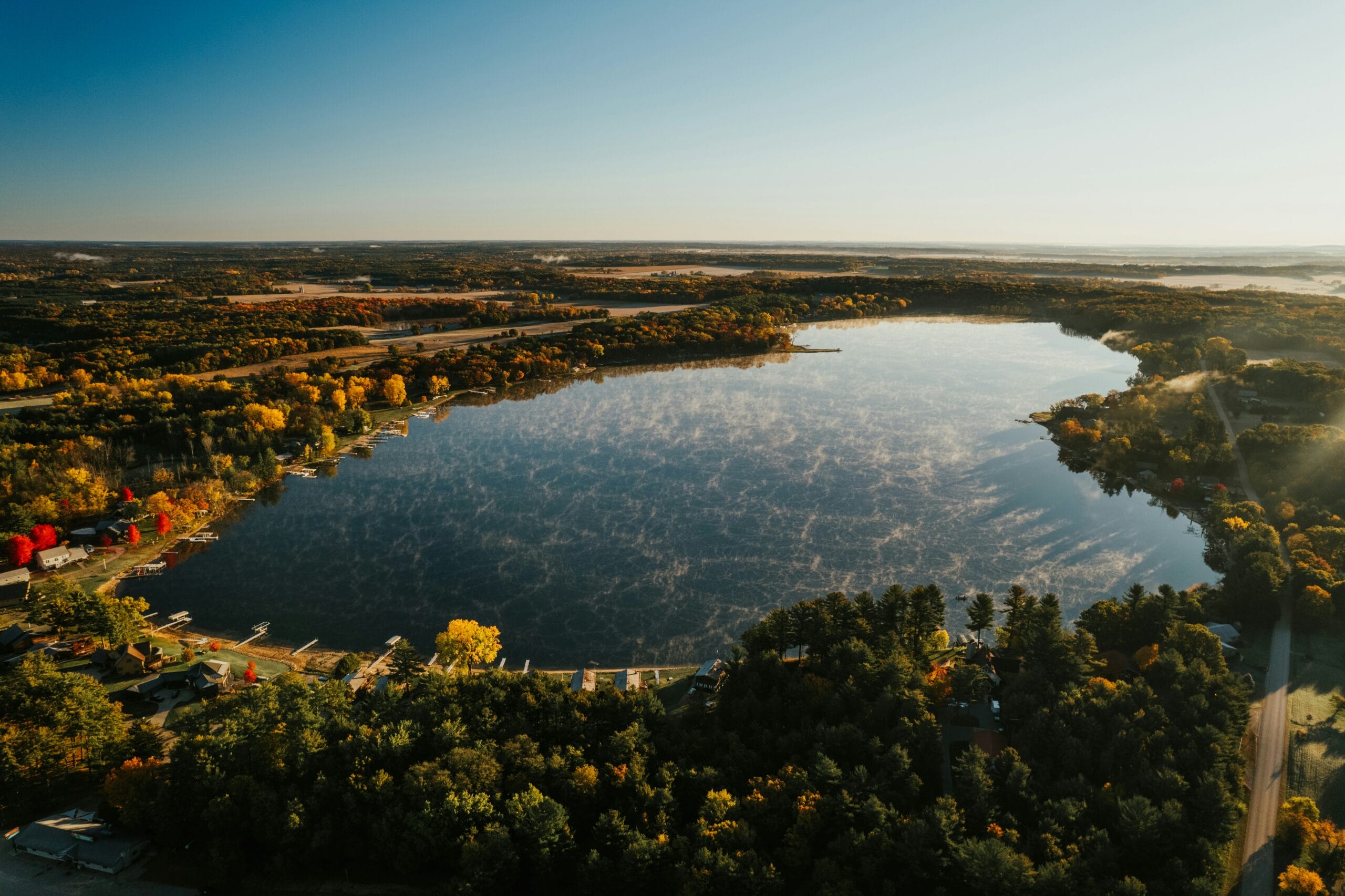 Aerial view of a serene lake surrounded by vibrant autumn foliage and reflections on the water's surface.