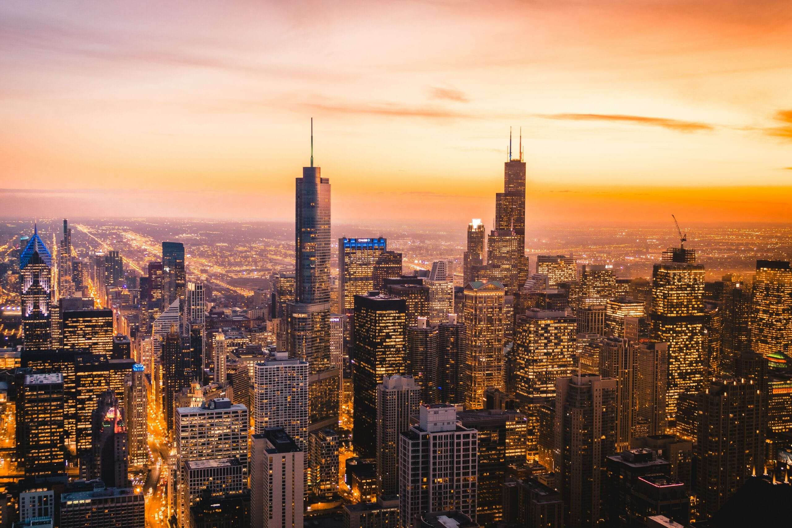 Chicago skyline at sunset, featuring illuminated skyscrapers and a gradient sky of orange and purple hues.