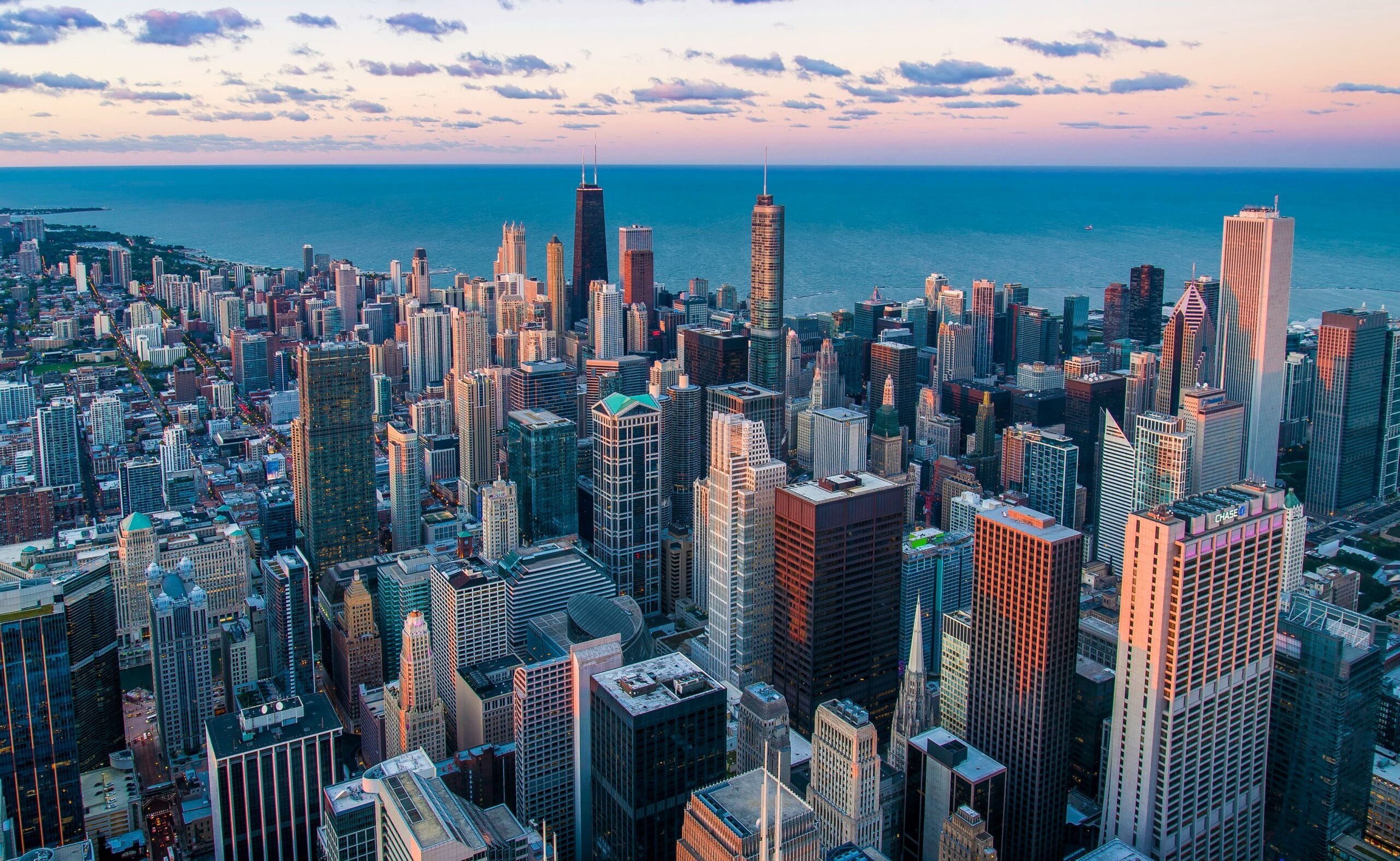 Aerial view of Chicago's skyline at sunset, featuring tall buildings and Lake Michigan in the background.