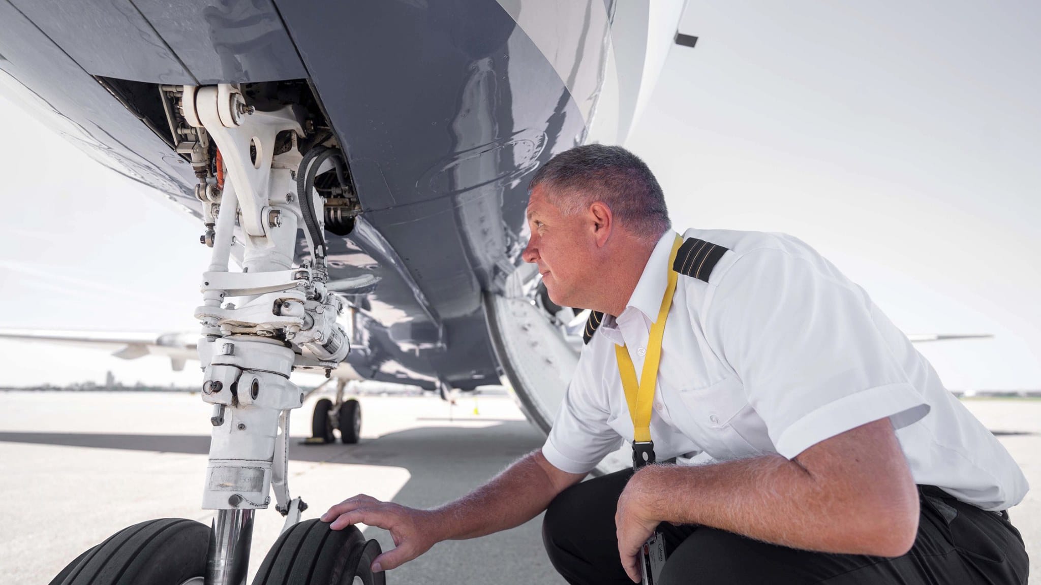 A pilot inspects the landing gear of an aircraft, focusing on the wheels and mechanical components.