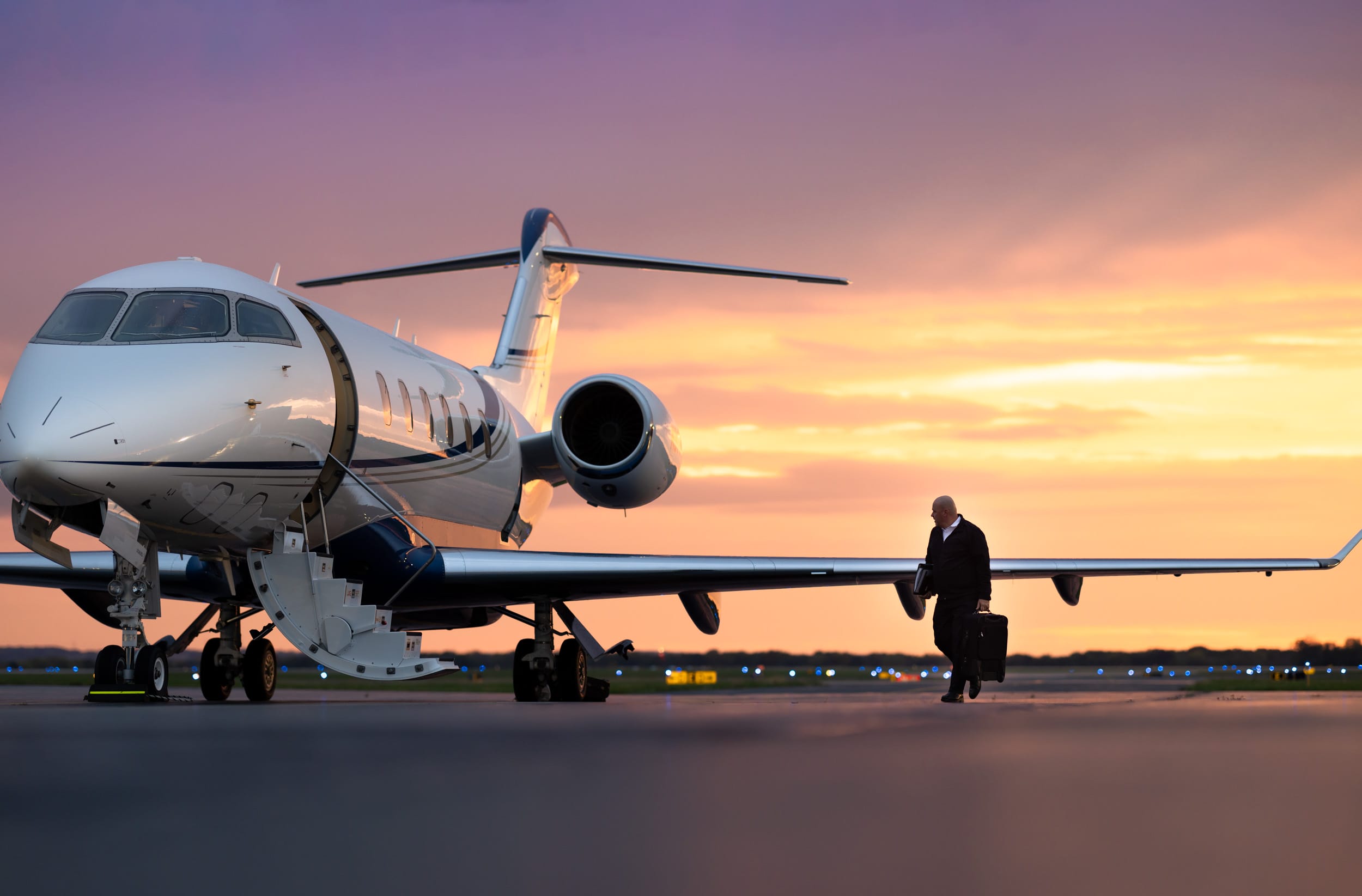 Businessman walking towards a private jet at sunset, with vibrant orange and purple skies in the background.