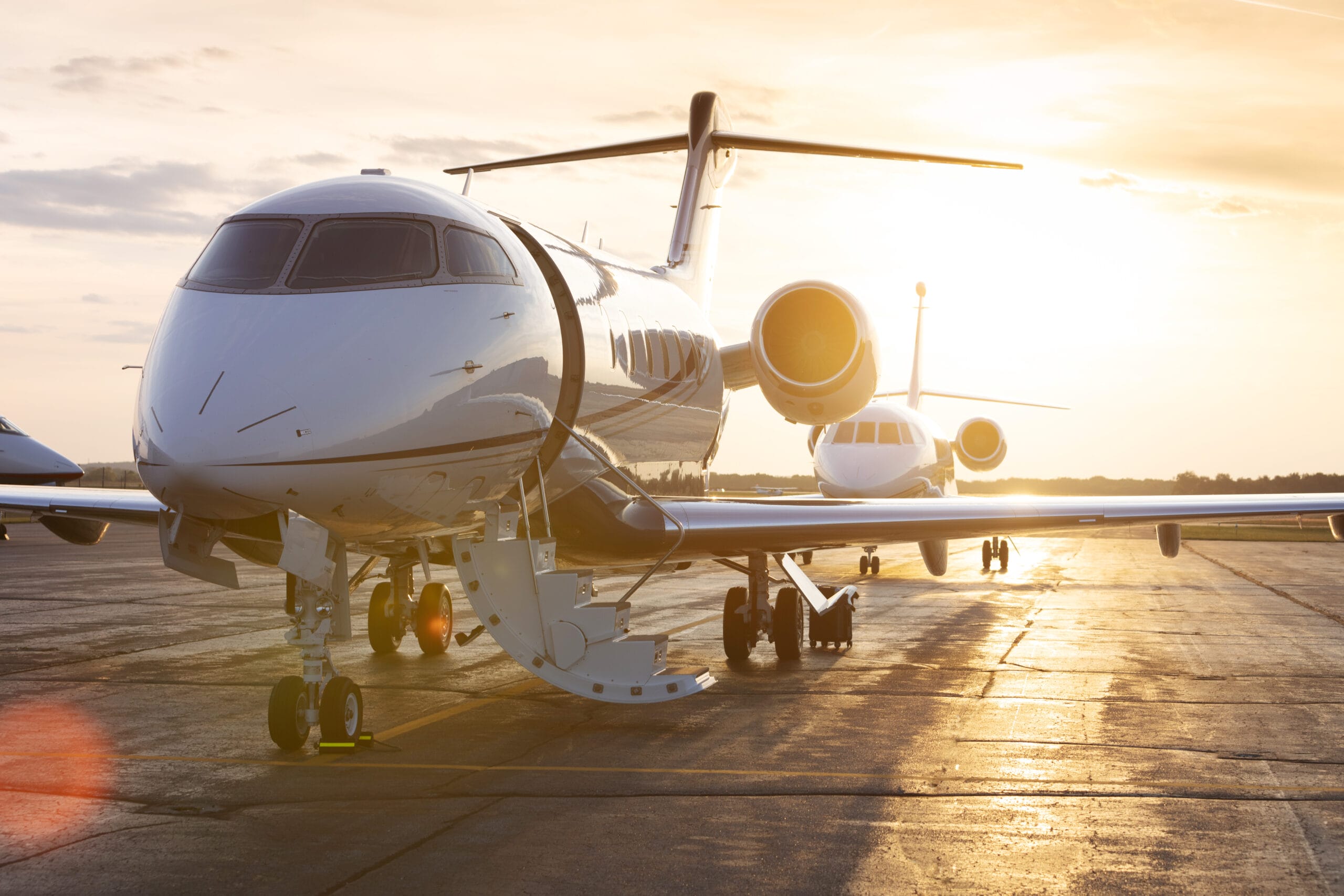 Two sleek private jets parked on a runway, illuminated by a warm sunset glow.
