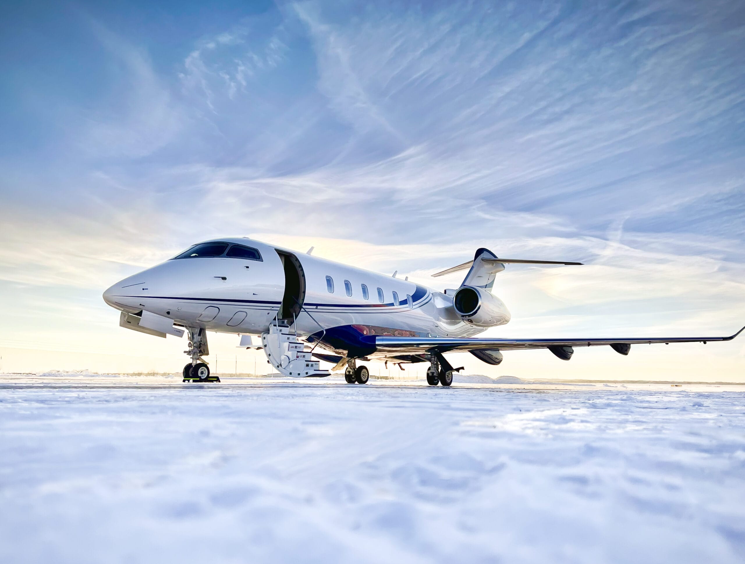 Private jet parked on a snowy runway, with a clear blue sky and wispy clouds in the background.