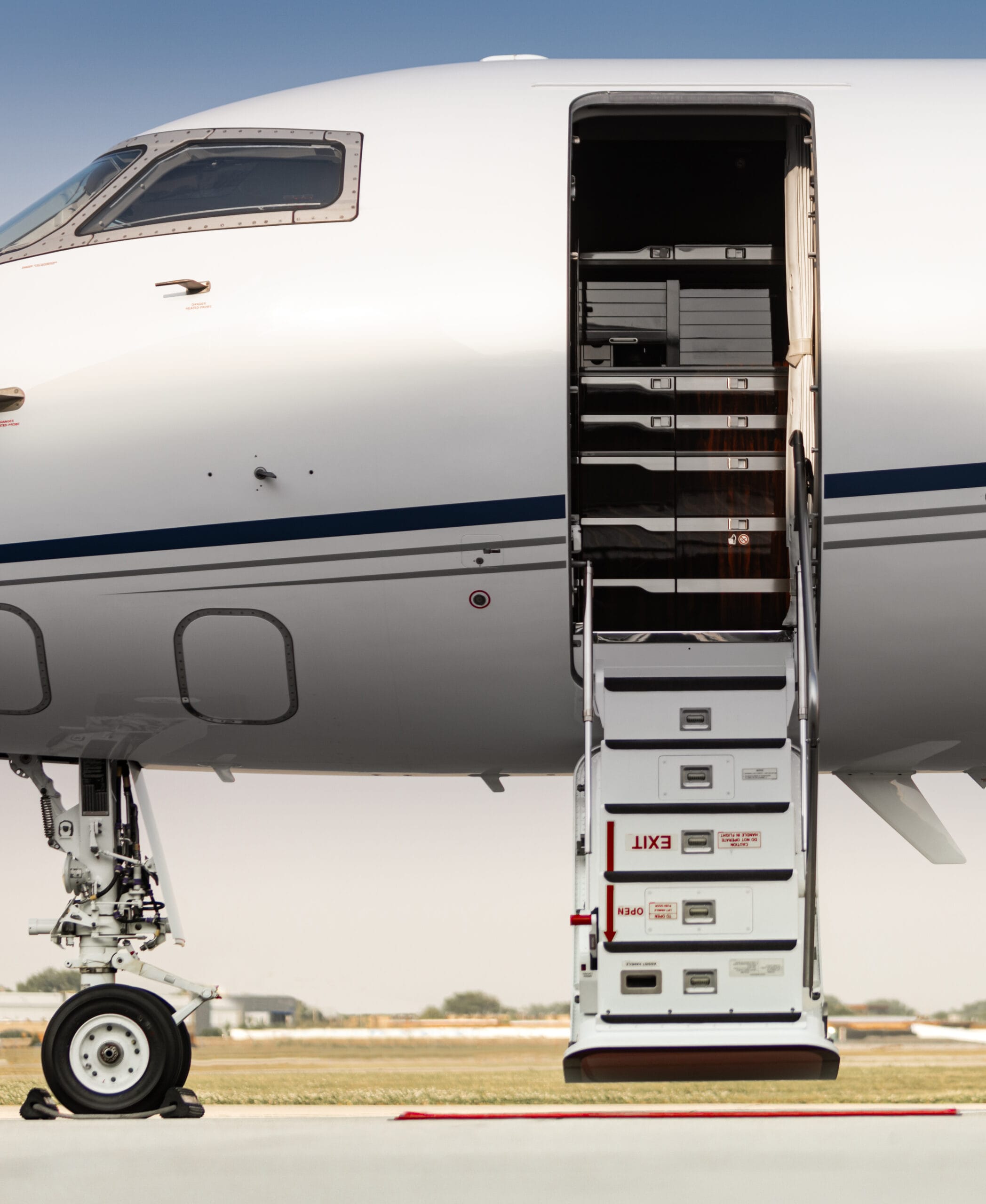 A private jet's open door with stairs leading down, showcasing sleek design and polished exterior against a clear sky.