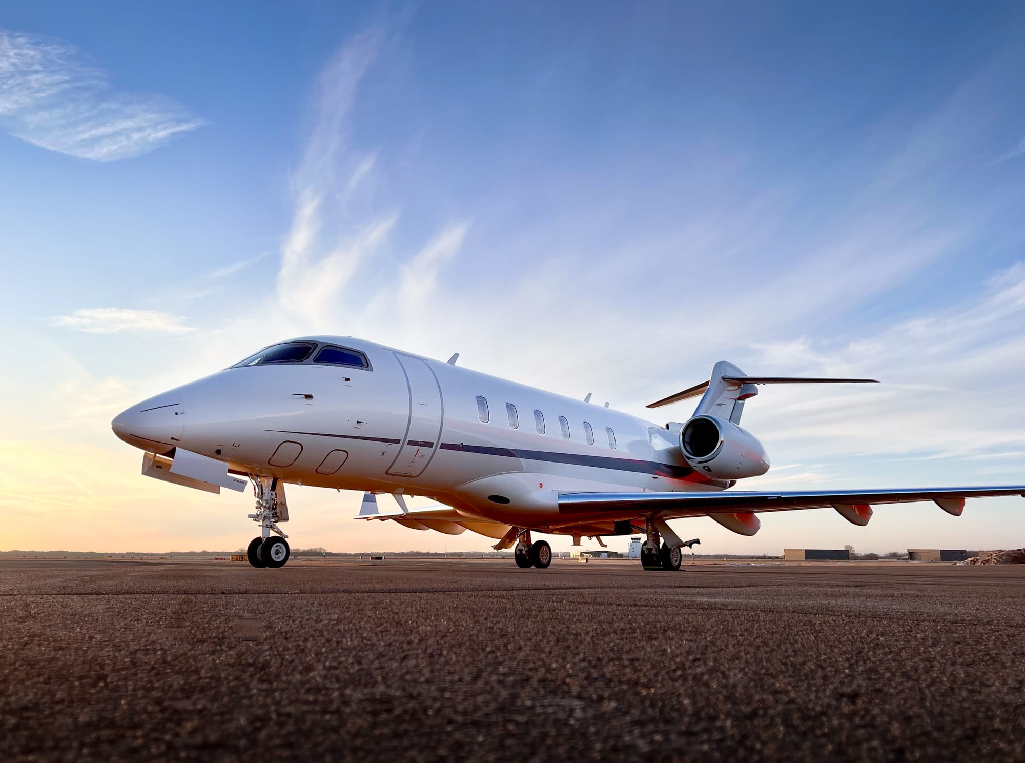 Private jet parked on an airstrip, with a clear blue sky and wispy clouds in the background.