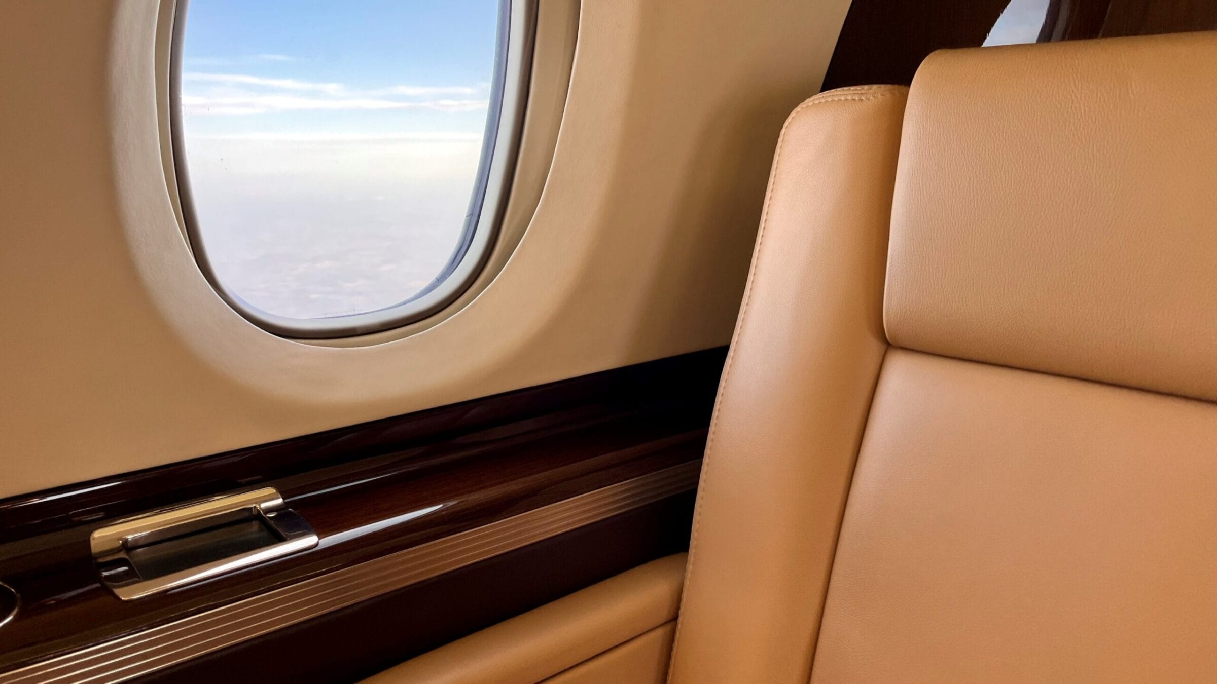 Luxury airplane interior featuring a plush tan seat and a large window revealing a clear blue sky.