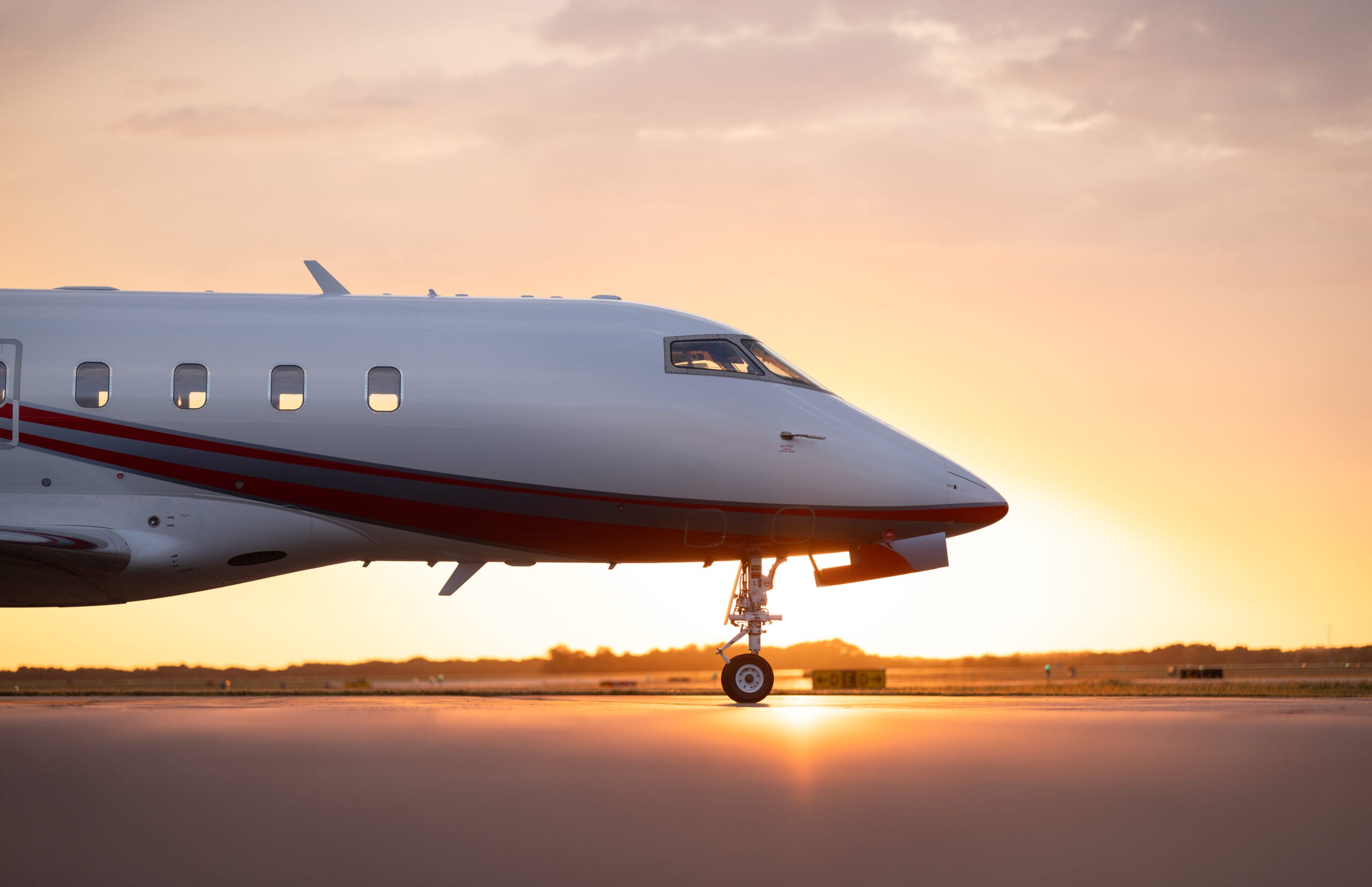 Private jet on the runway, illuminated by a warm sunset, showcasing its sleek design and reflective surface.