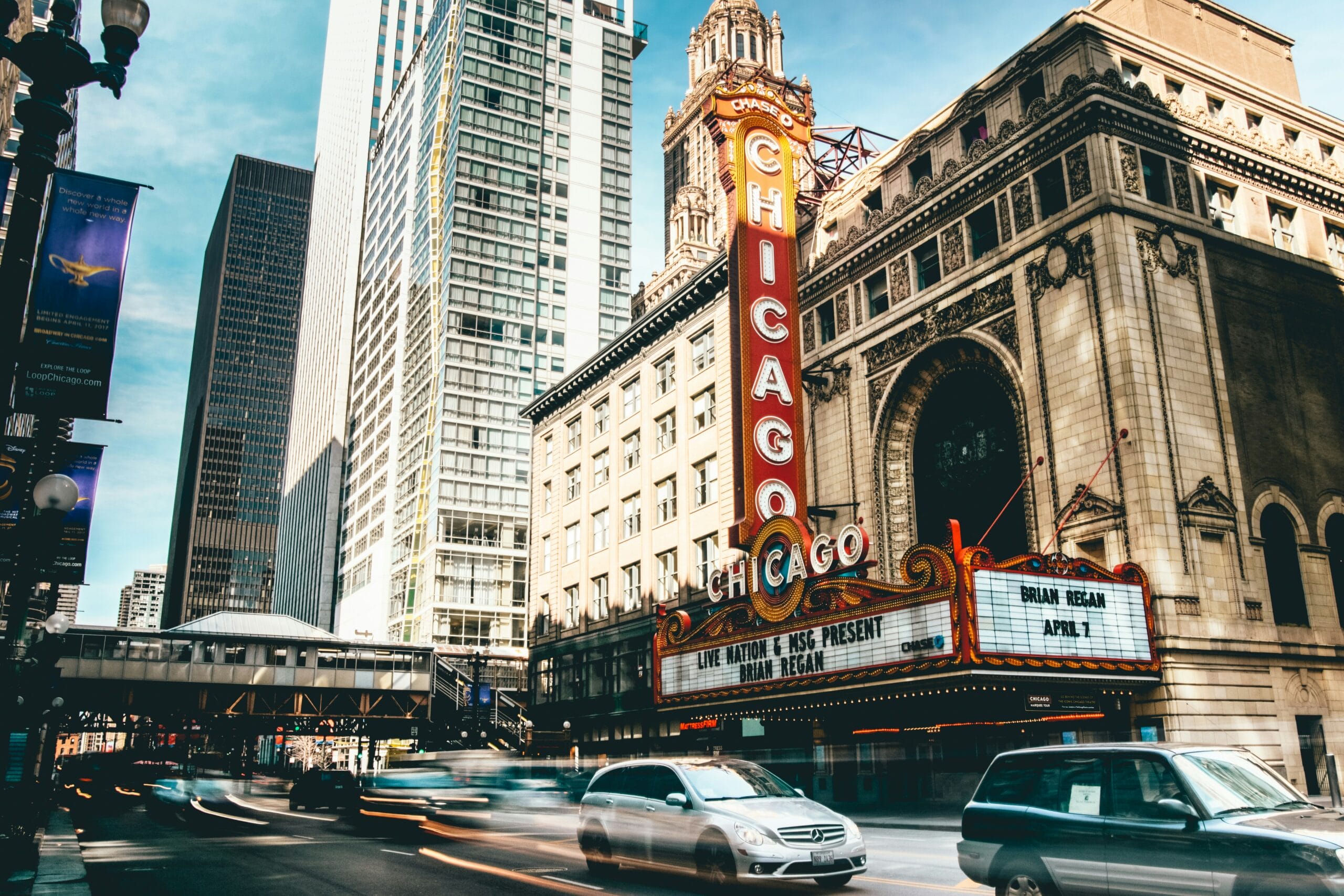 Chicago Theatre marquee with skyscrapers and traffic on a sunny day.