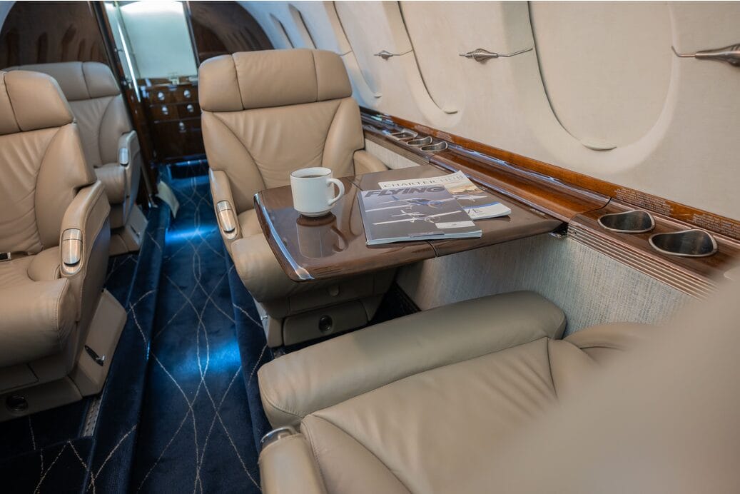 Luxury jet interior with leather seats, a coffee cup, and magazines on a tray table.