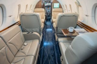 Luxurious private jet interior with leather seats, blue carpet, and a coffee cup.