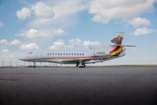 White jet airplane with colorful stripe and tail logo on tarmac under cloudy sky.