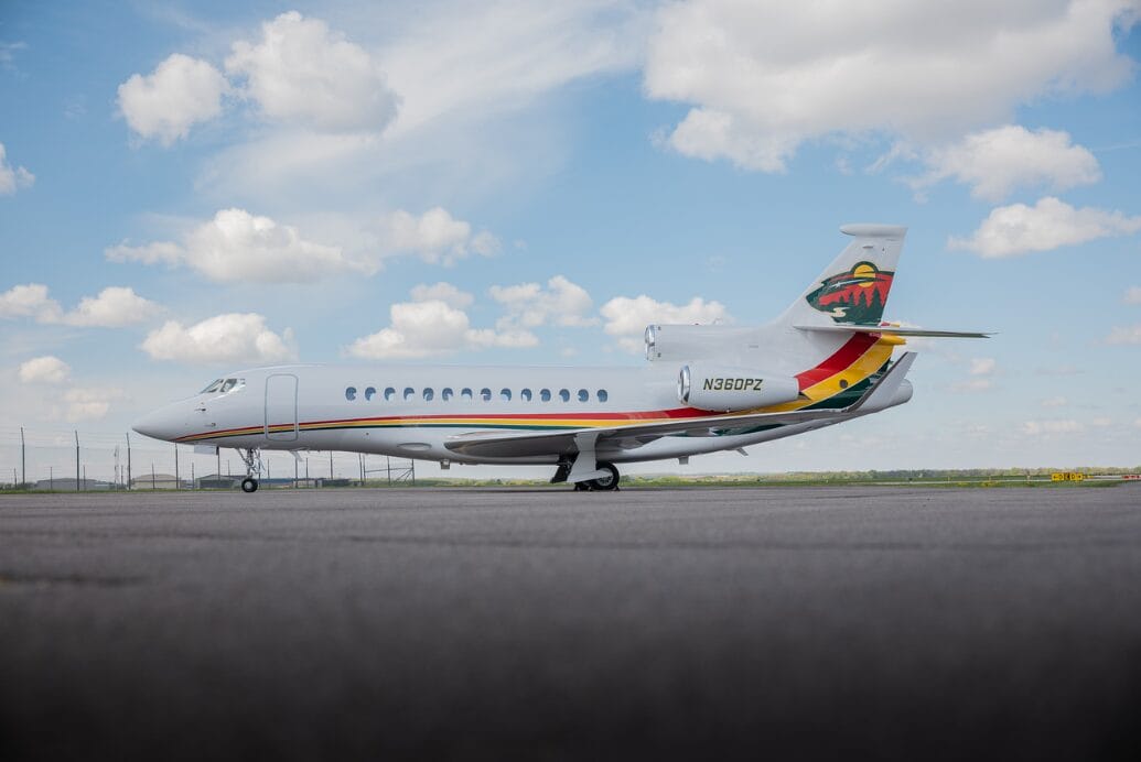 White jet airplane with colorful stripe and tail logo on tarmac under cloudy sky.