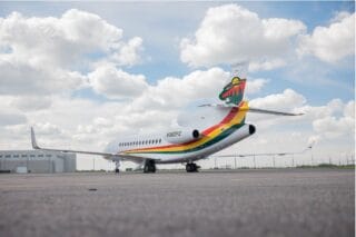 Private jet with colorful livery and a forest logo on the tail, parked on tarmac.