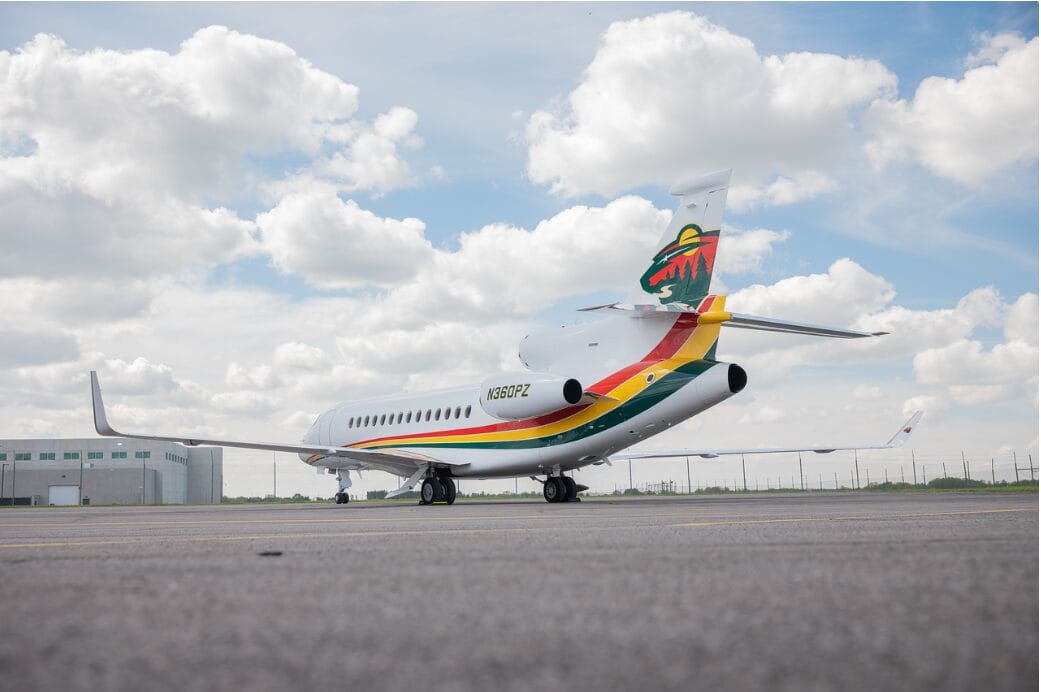 Private jet with colorful livery and a forest logo on the tail, parked on tarmac.