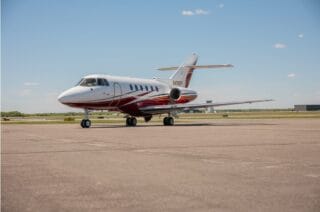 White and red private jet parked on tarmac under a blue sky.