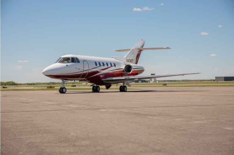 White and red private jet parked on tarmac under a blue sky.