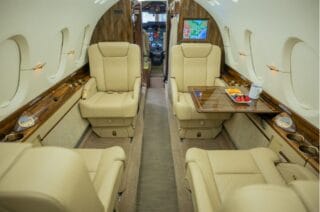 Luxurious private jet interior with cream leather seats, wood accents, and a tray of fruit.
